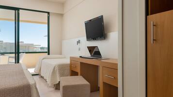 A hotel room with two beds, a desk with a laptop, a TV, and a sliding door to a balcony.