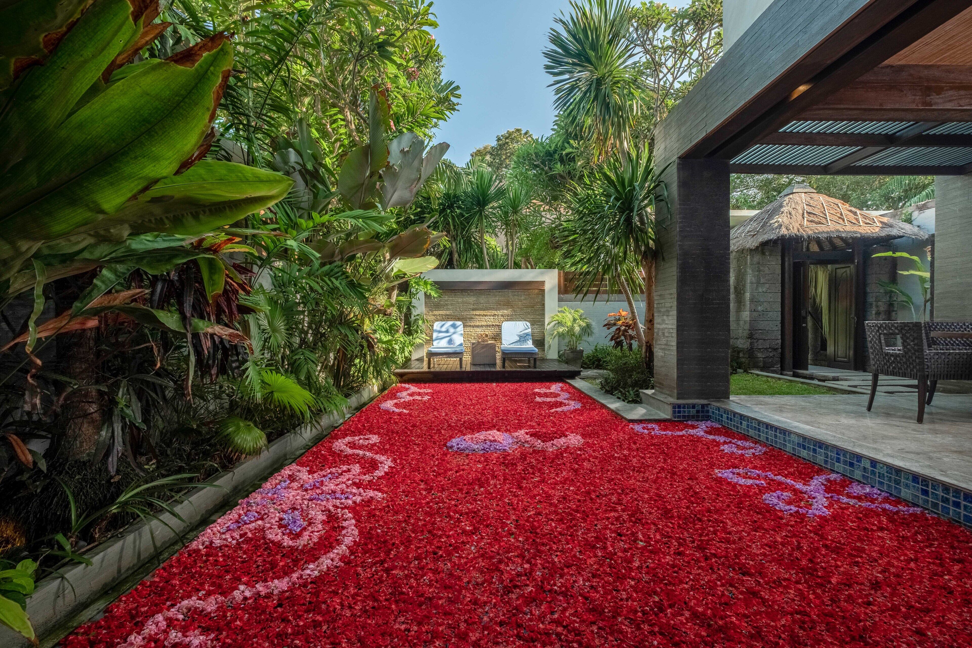 Un chemin de jardin orné de motifs floraux rouges et blancs mène à un espace de détente comprenant deux chaises et une table.
