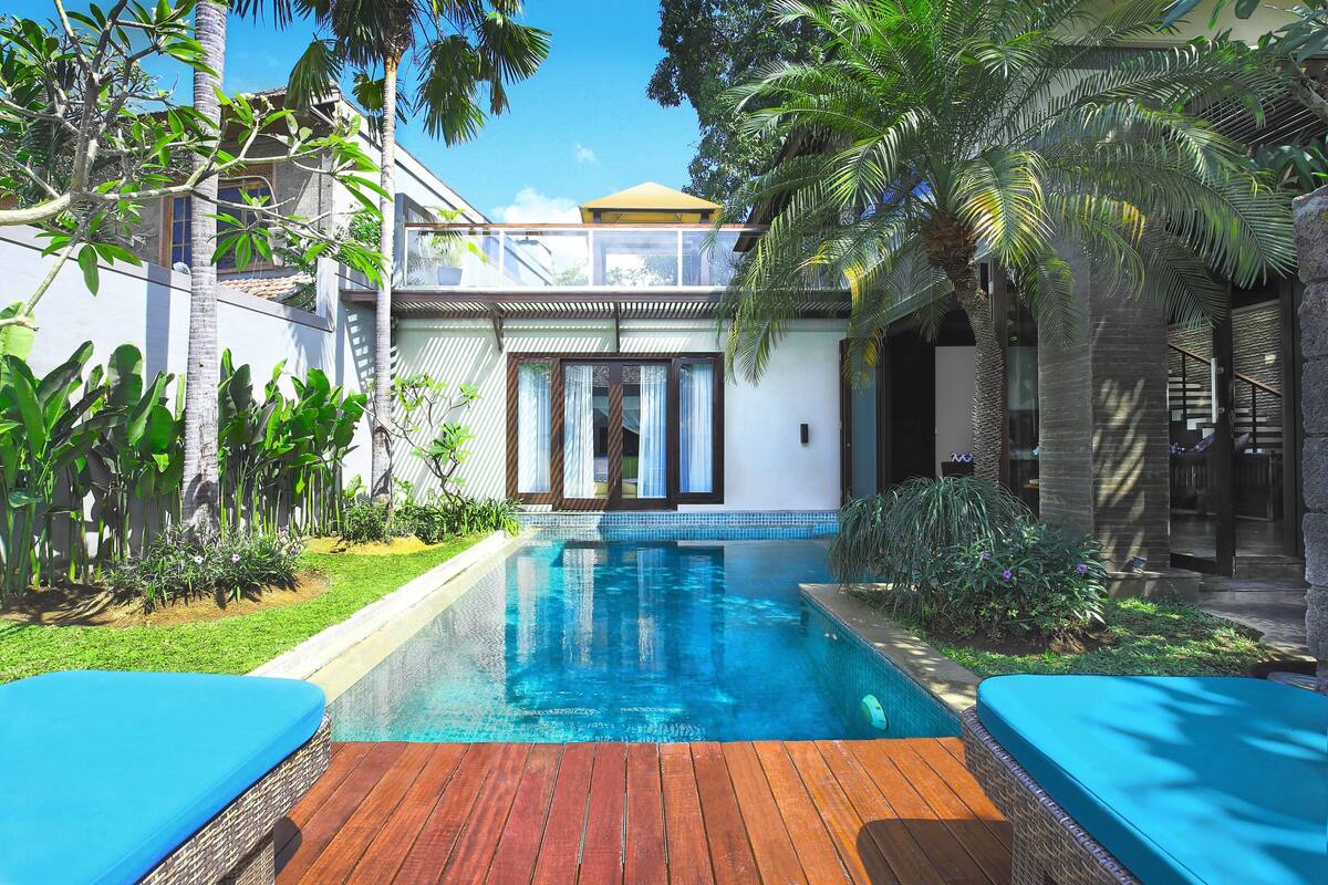 A pool area with wooden decking, a clear blue pool, and a small garden with tropical plants.