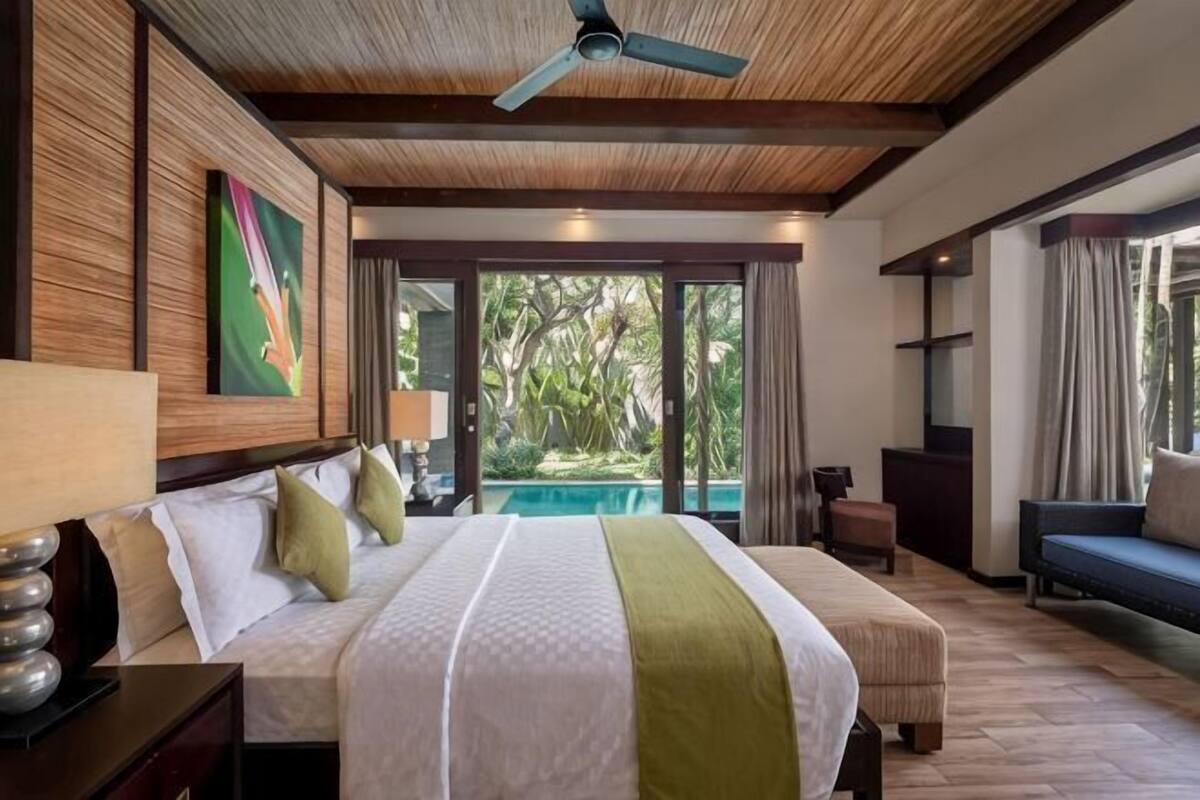 A bedroom with a bed, bedside table, lamp, and a view of a pool.
