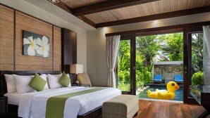 A hotel room with a bed, a nightstand, a lamp, a window with a view of a pool and greenery, and a duck float. - Le Jardin Villas Seminyak (Seminyak)