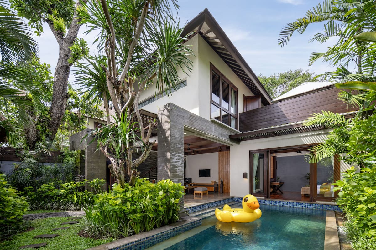 A modern house with a swimming pool, surrounded by lush greenery and palm trees.