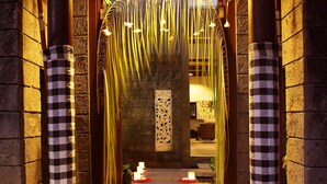 A corridor with a stone floor, candles, and flower petals leading to a room with a thatched roof. - Le Jardin Villas Seminyak (Seminyak)