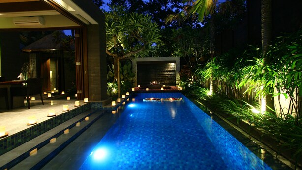 A swimming pool with a tiled edge, surrounded by lush greenery and palm trees. - Le Jardin Villas Seminyak (Seminyak)