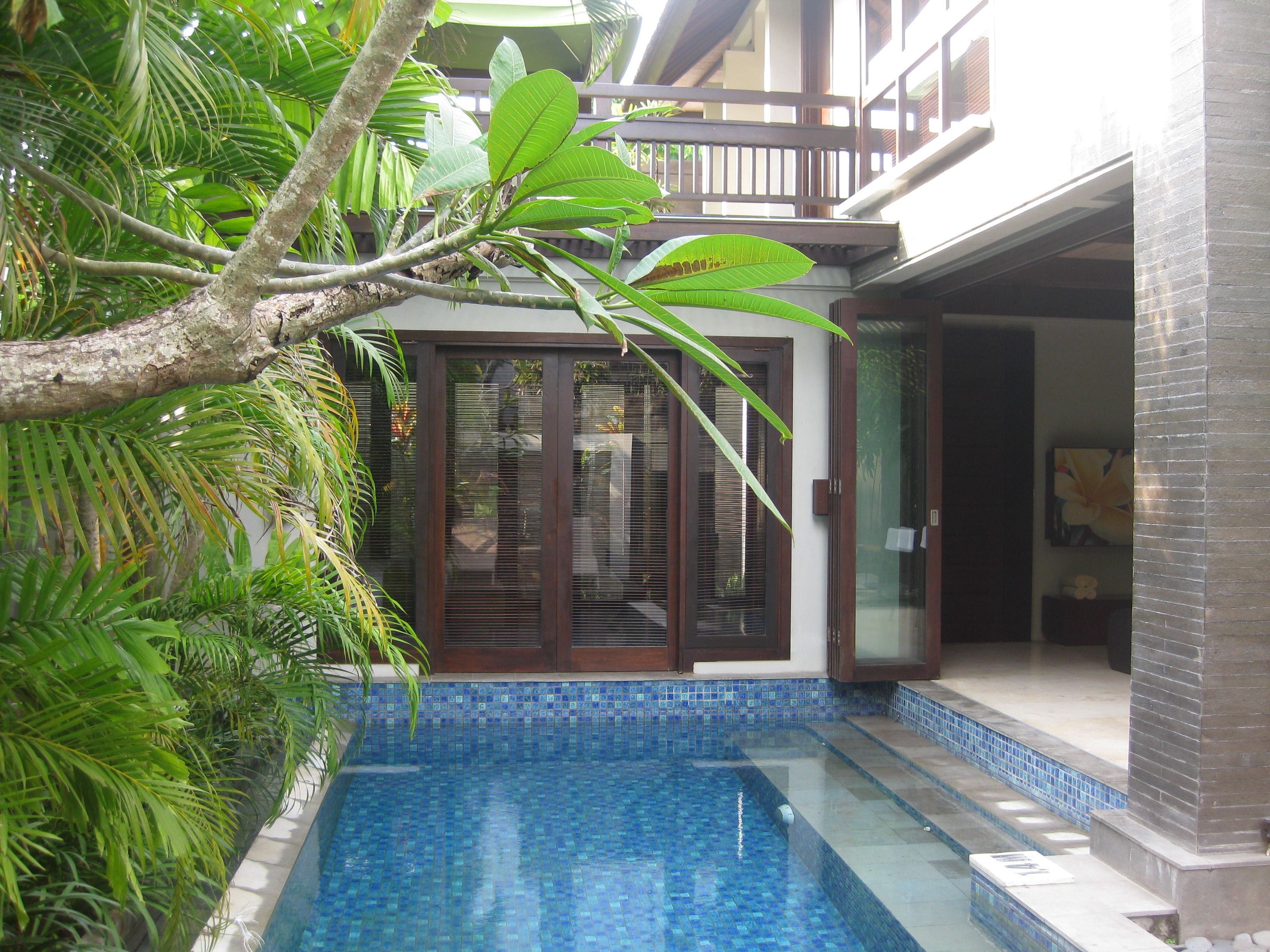 A pool area with a tiled edge, surrounded by lush greenery and a building with a balcony.