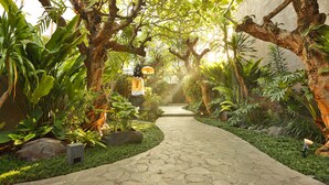 A stone pathway leading through a lush garden with various plants and trees. - Le Jardin Villas Seminyak (Seminyak)