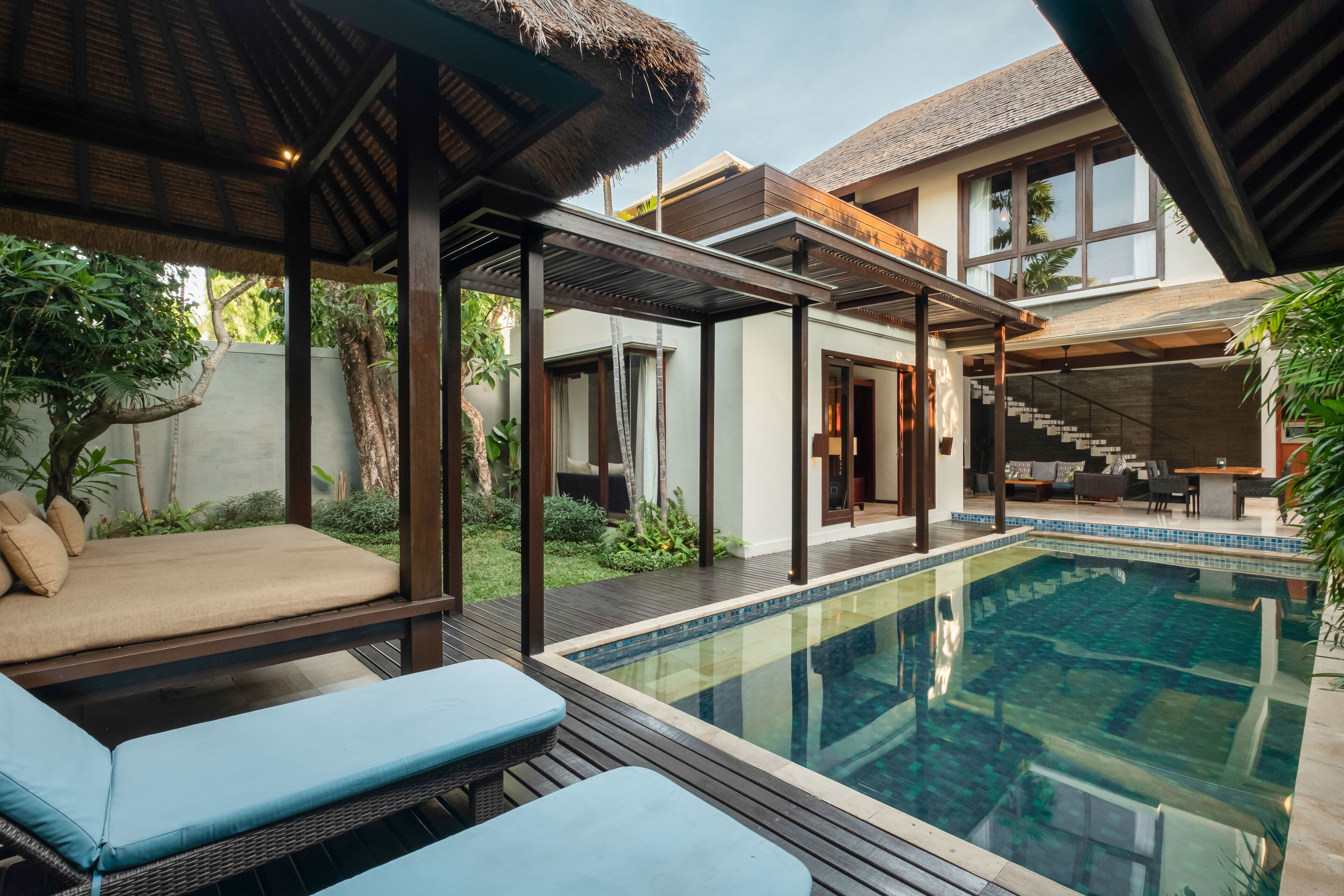 A poolside area with lounge chairs, a covered seating area, and a staircase leading to a second floor.