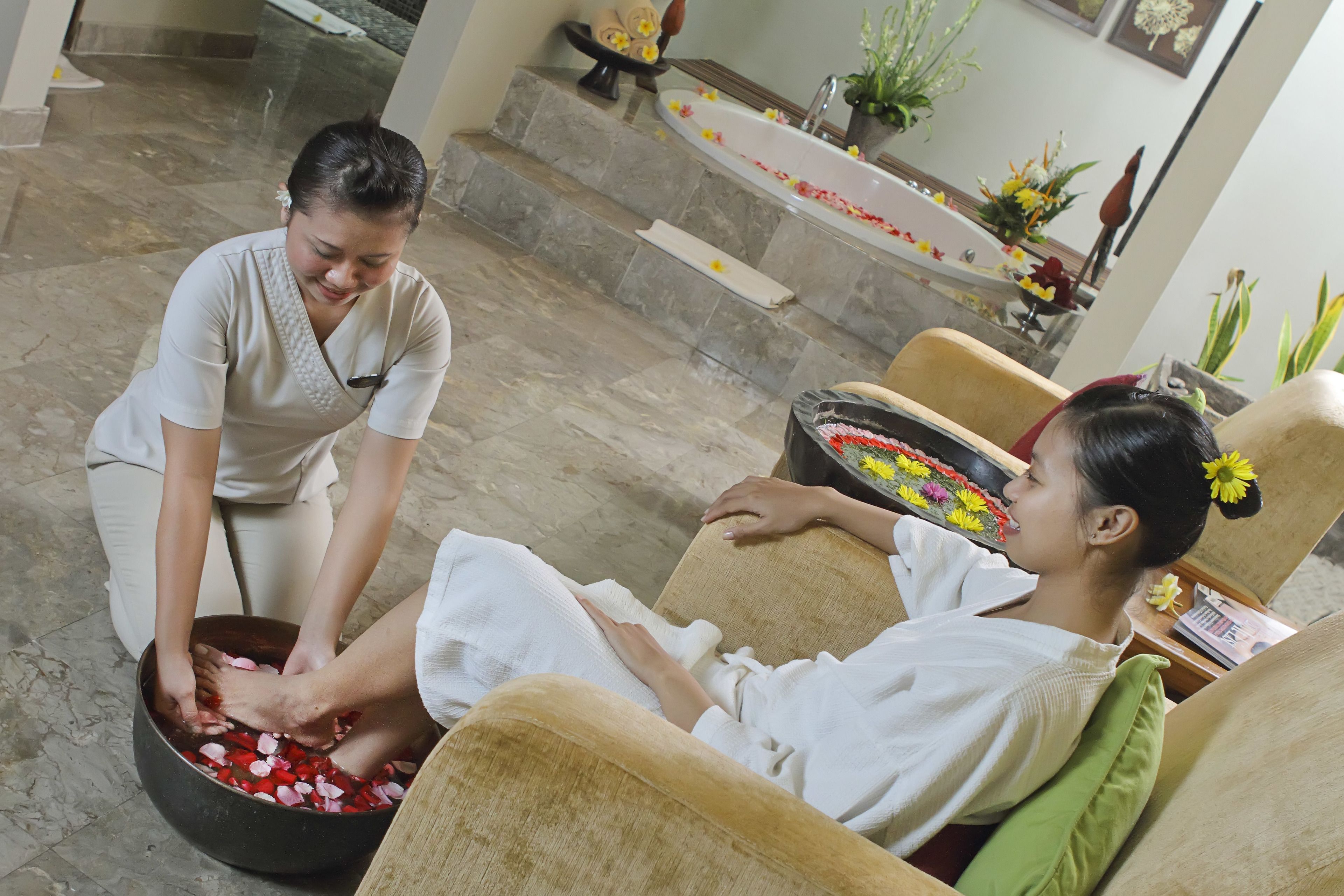 A spa setting with a massage table, a bowl of rose petals, and a bathtub with flowers.