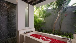 A modern bathroom with a large bathtub filled with red rose petals, a shower area with mosaic tiles, and lush greenery outside. - Le Jardin Villas Seminyak (Seminyak)