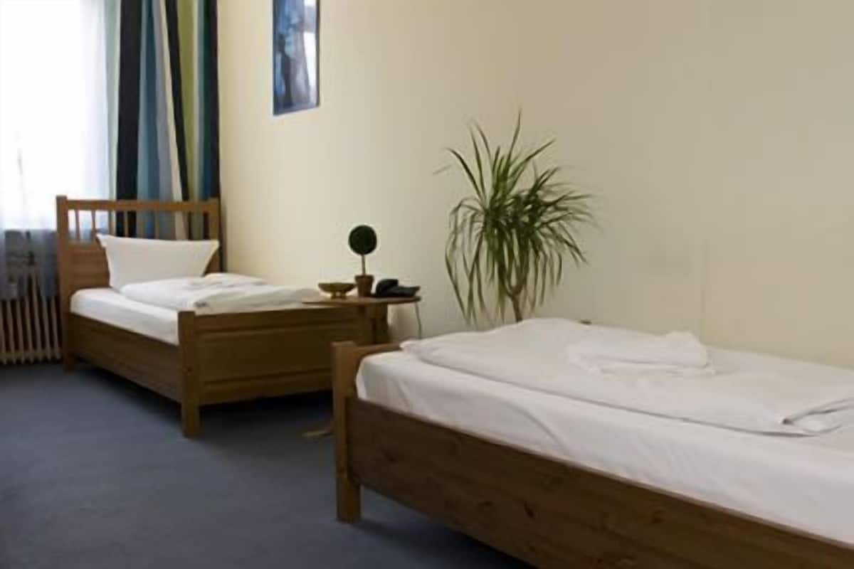 Deux lits en bois dans une pièce équipée d’un radiateur, d’une petite table avec une lampe et d’une plante en pot.