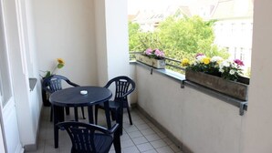 A small balcony with a round table and four chairs, a flower planter with various flowers, and a view of buildings and greenery in the background. - Hotel Pension Rheingold (Berlin)