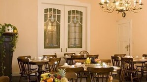 A dining area with round tables, wooden chairs, and a chandelier. - Hotel Pension Rheingold (Berlin)
