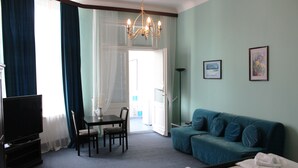 A hotel room with a bed, a TV, a desk with a chair, a sofa, and a chandelier. - Hotel Pension Rheingold (Berlin)