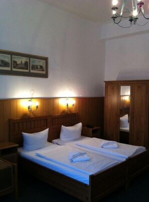 Una habitación de hotel con una cama de madera, dos mesitas de noche, un armario de madera y una araña.