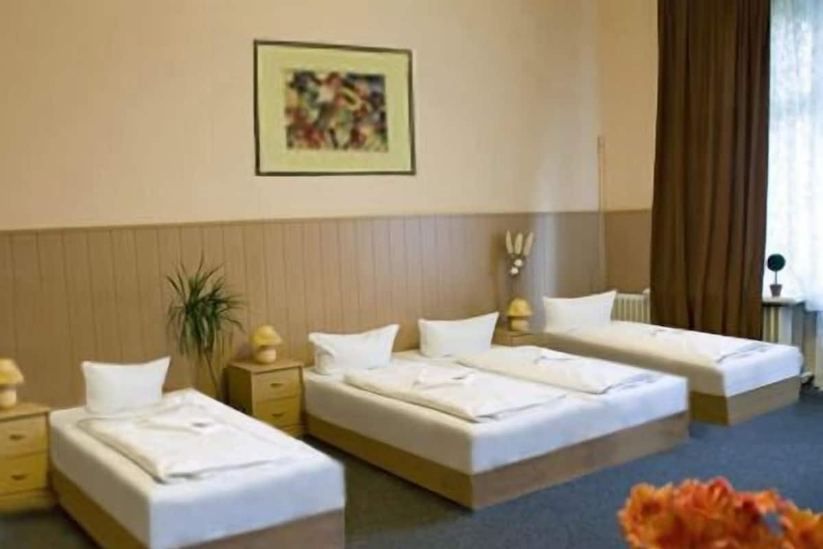 Une chambre d’hôtel avec trois lits, une table de chevet avec une lampe, une plante et un tableau encadré au mur.