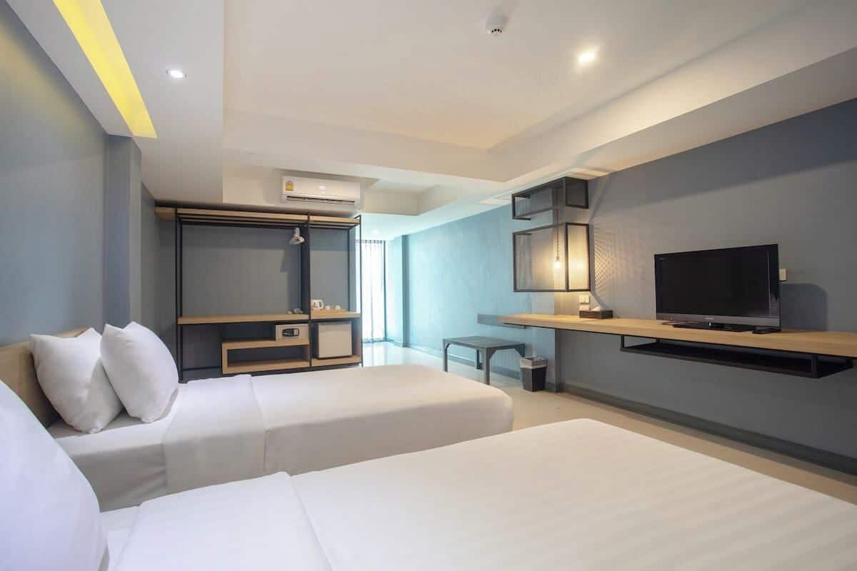 A modern hotel room with two beds, a TV, a desk, and a large window.