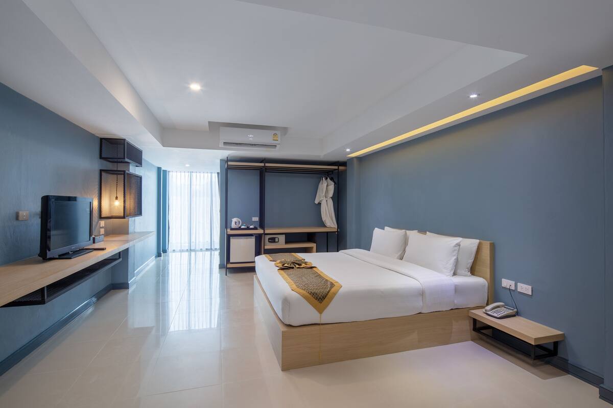 A modern hotel room with a bed, bedside table, TV, and a walk-in closet.
