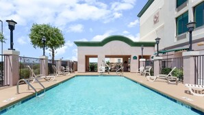 A swimming pool with lounge chairs and a building with a green roof in the background. - Wingate by Wyndham Yuma (Yuma)