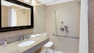 A bathroom with a granite countertop sink, a mirror, a handheld showerhead, and a grab bar.