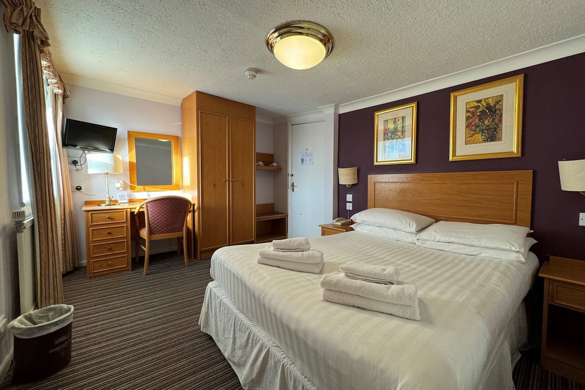 A hotel room with a bed, a desk, a chair, a wardrobe, and a television.