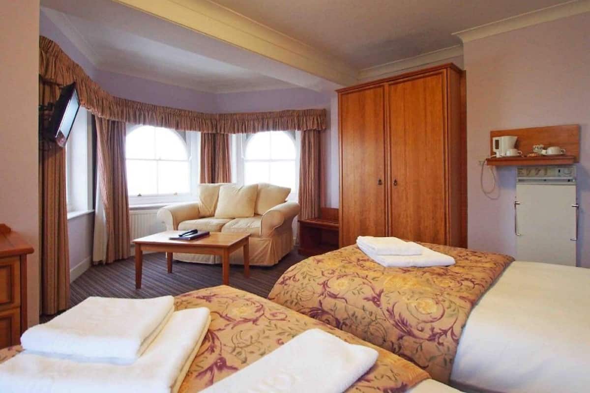 A hotel room with two beds, a sofa, a TV, and a wardrobe.