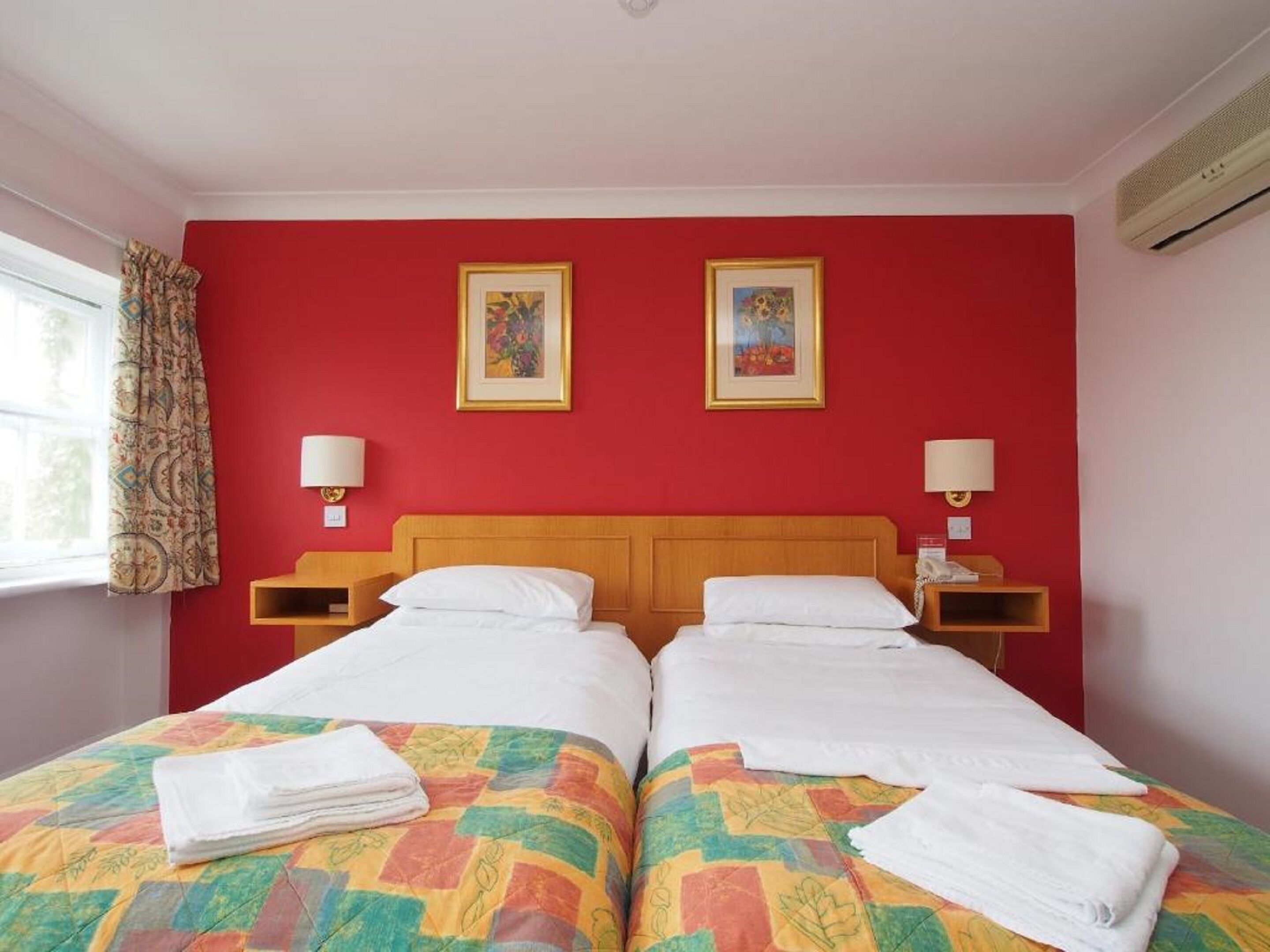 A hotel room with two beds, red walls, and two framed pictures.