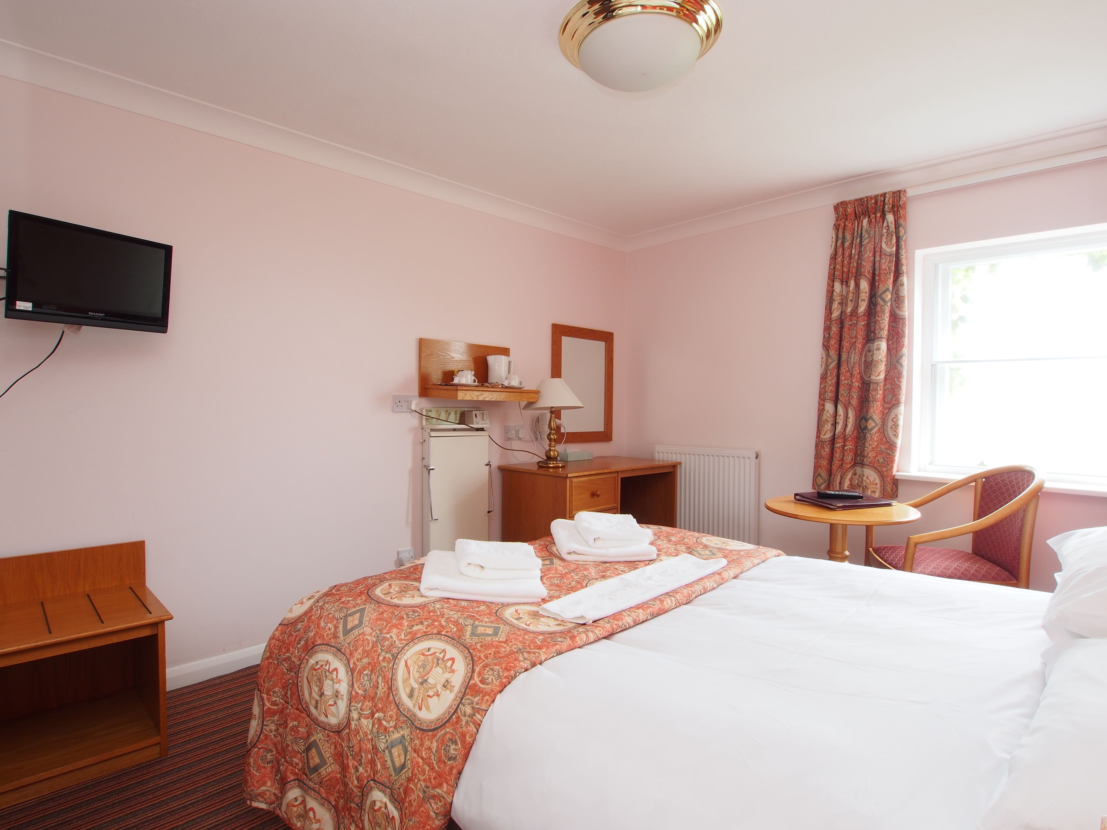 A hotel room with a bed, a desk, a chair, a television, and a window with curtains.