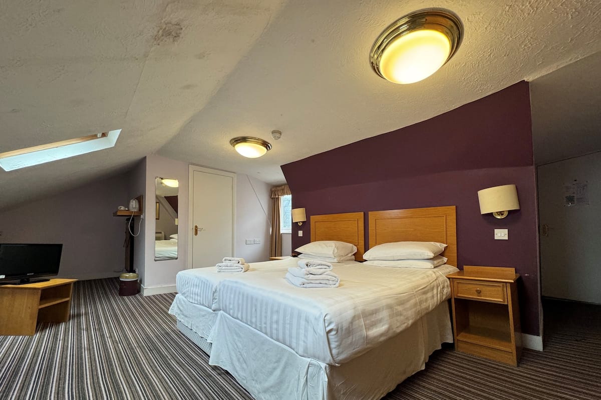 A hotel room with a large bed, two bedside tables, a TV, and a ceiling light.