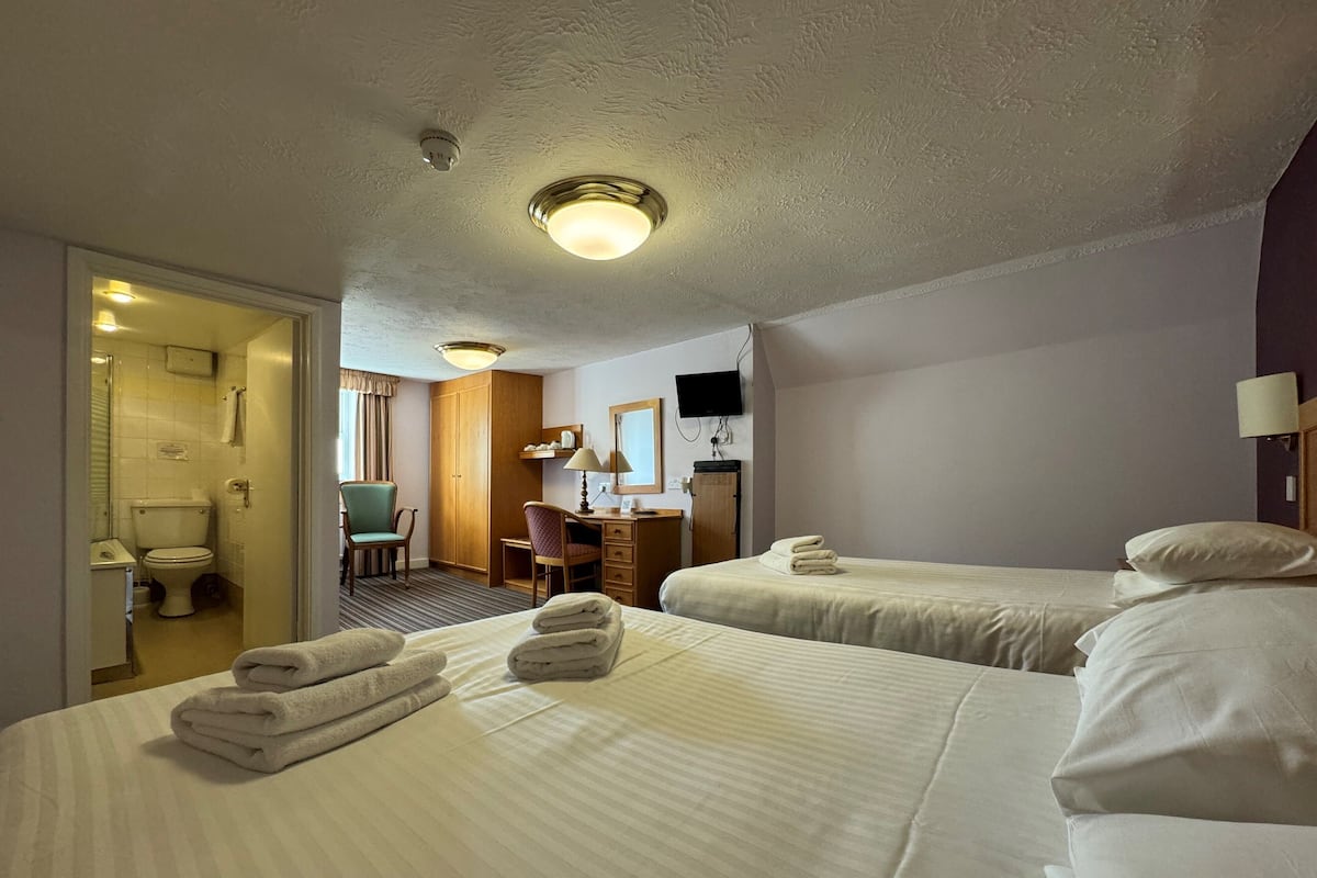 A hotel room with two beds, a desk, a chair, a TV, and a bathroom visible through an open door.