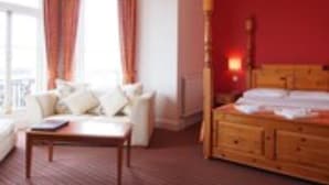 A hotel room with a large bed, a sitting area with a sofa and armchairs, and a view of the outdoors. - Chatsworth Hotel - Worthing (Worthing)