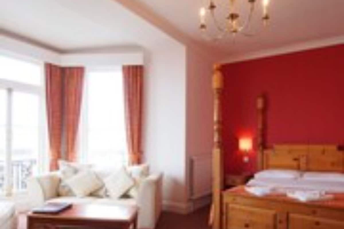 A hotel room with a large bed, a sitting area with a sofa and armchairs, and a view of the outdoors.