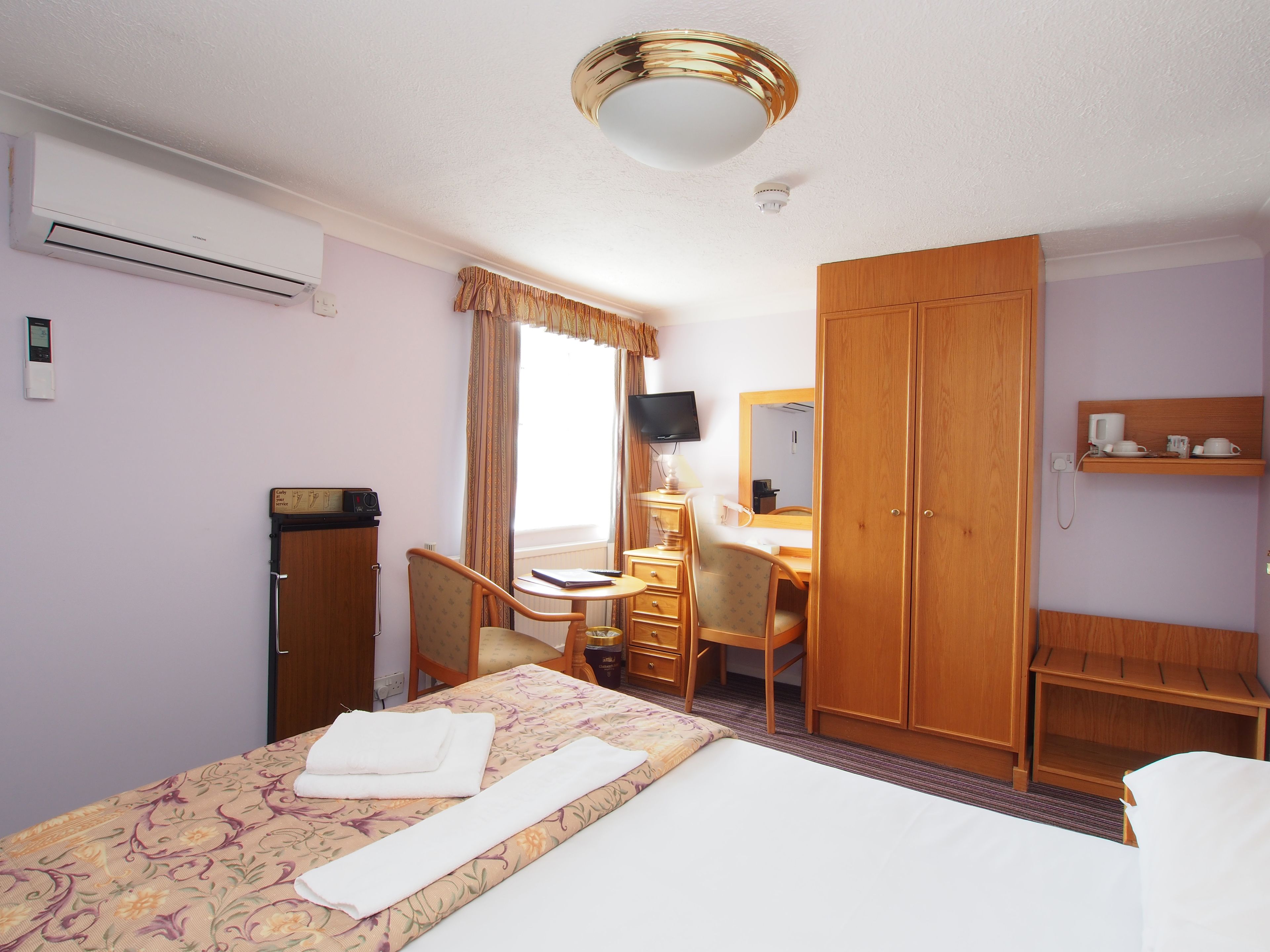 A hotel room with a bed, a desk, a chair, a wardrobe, and a television.
