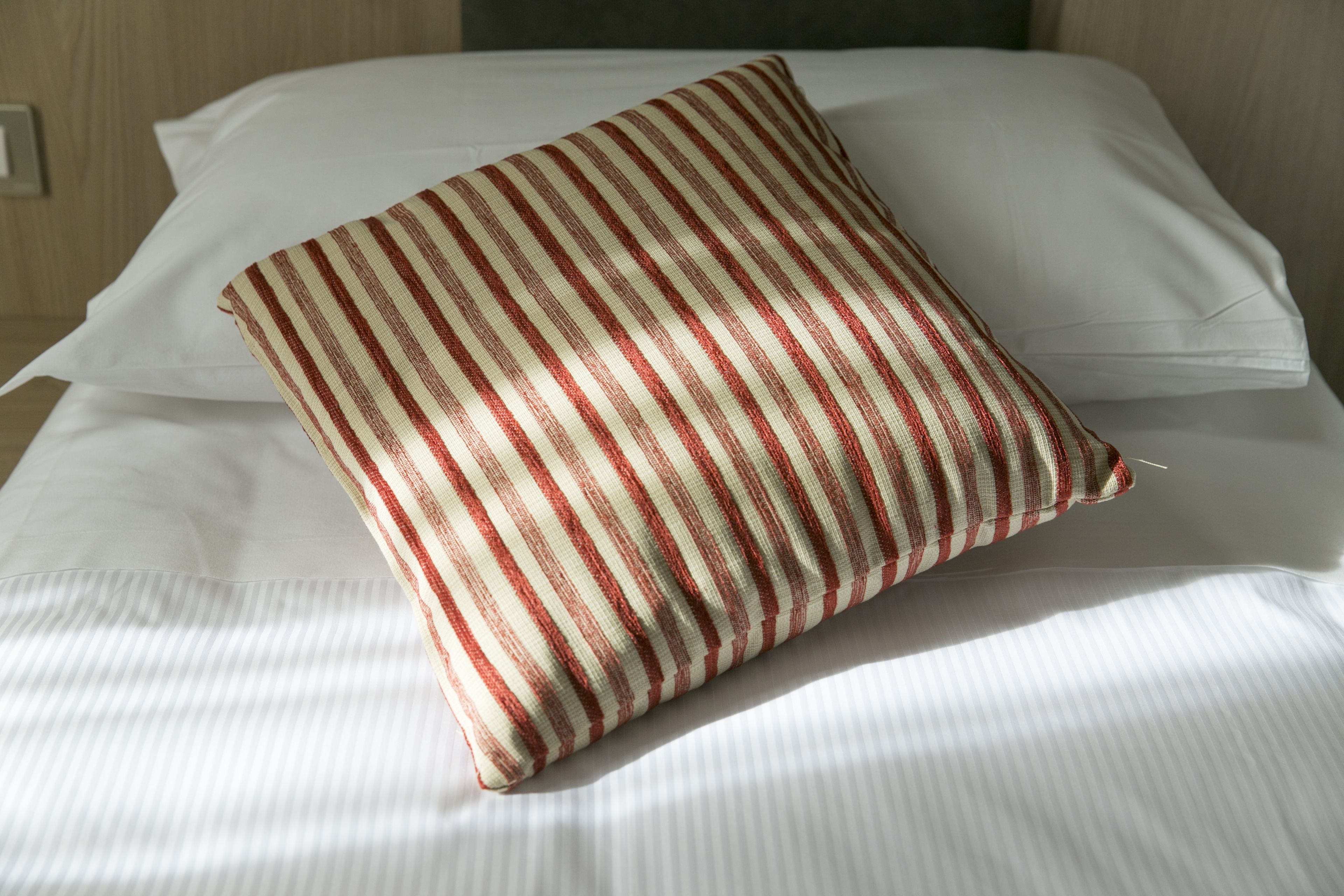 A bed with white linens and a striped pillow.
