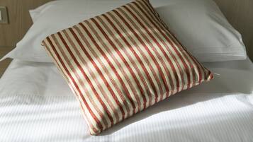 A bed with white linens and a striped pillow.