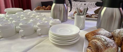 A breakfast buffet with coffee pots, plates, and pastries.