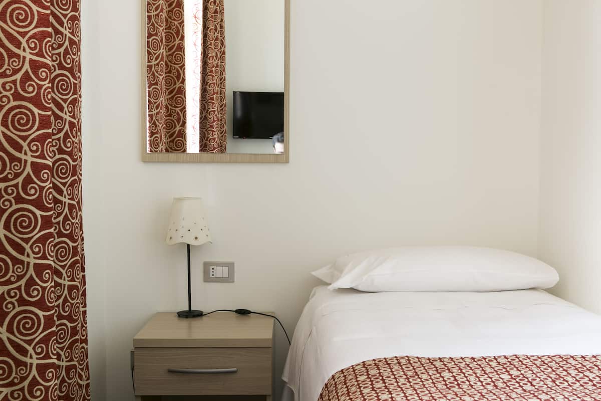 A hotel room with a bed, a nightstand with a lamp, a mirror, and a TV.