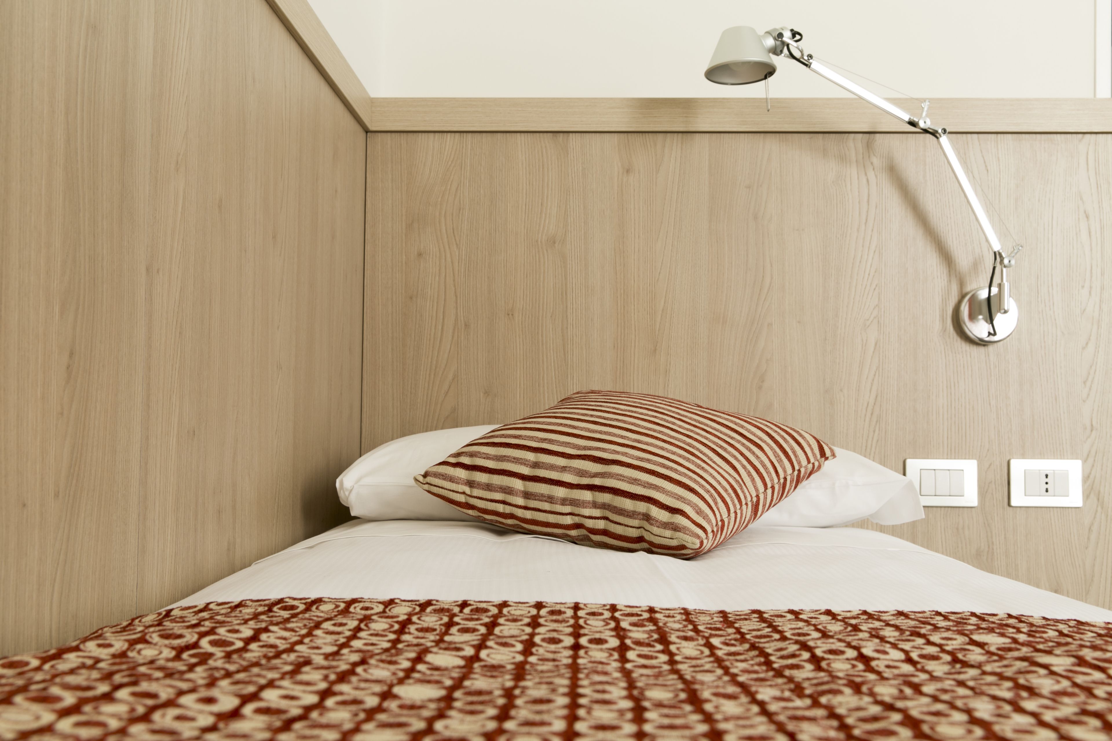 Una cama bien hecha con un edredón estampado, una almohada a rayas y una lámpara de noche.