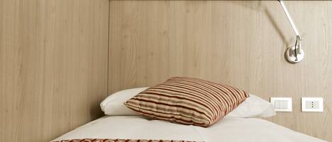 Una cama bien hecha con un edredón estampado, una almohada a rayas y una lámpara de noche.