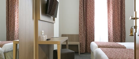 Ett hotellrum med två sängar, ett skrivbord med en stol, en TV och mönstrade gardiner.