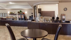 Um hall de hotel com uma mesa redonda e duas cadeiras, um balcão com diversos itens, e um relógio na parede.