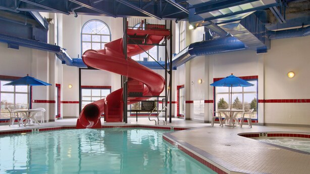 Piscina interna com escorregador vermelho, cadeiras de descanso e hidromassagem.