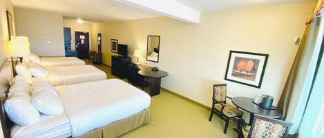 A hotel room with three beds, a desk, a chair, a small table, and a painting on the wall.