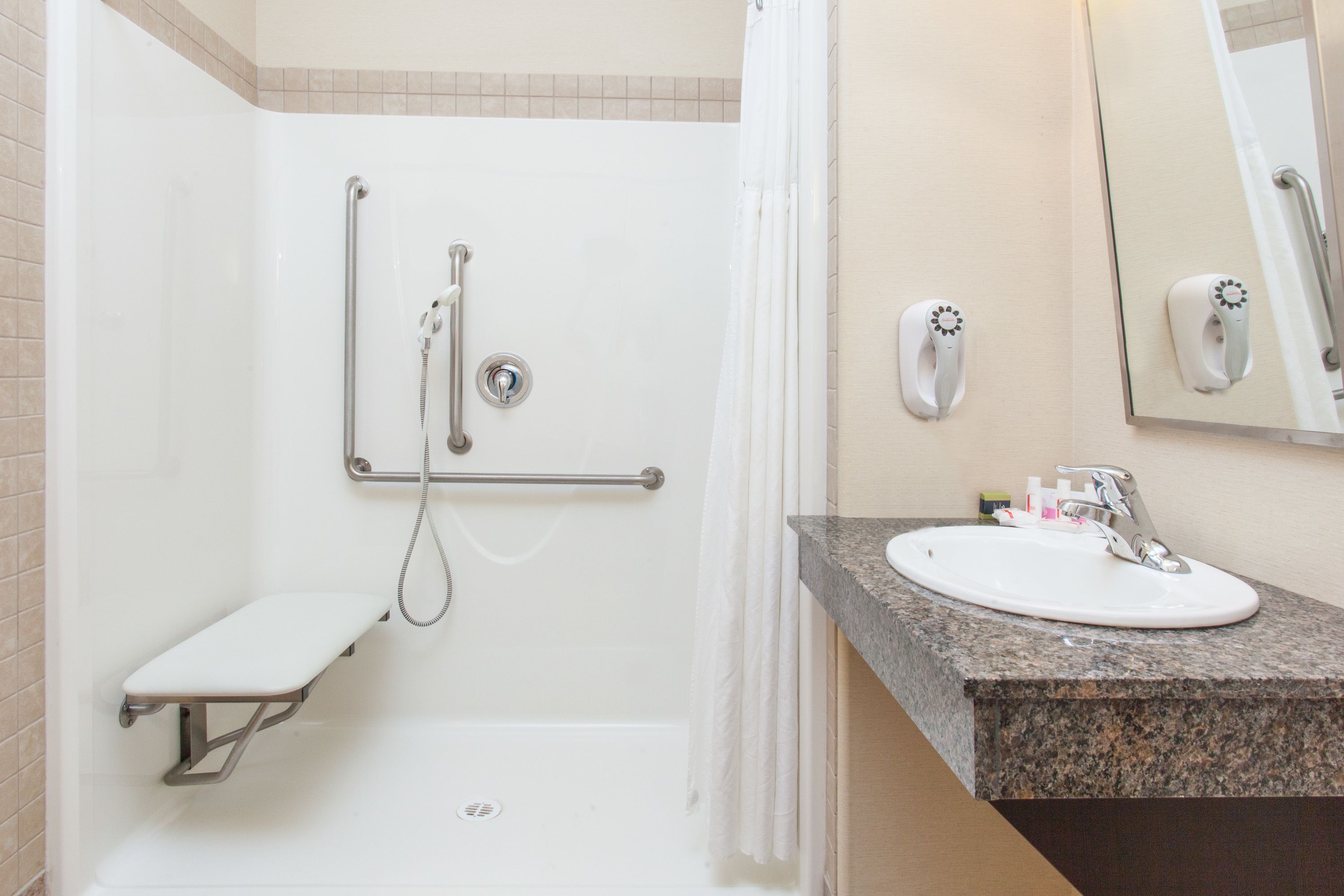 A bathroom with a shower, grab bar, bench, sink, and hand dryer.
