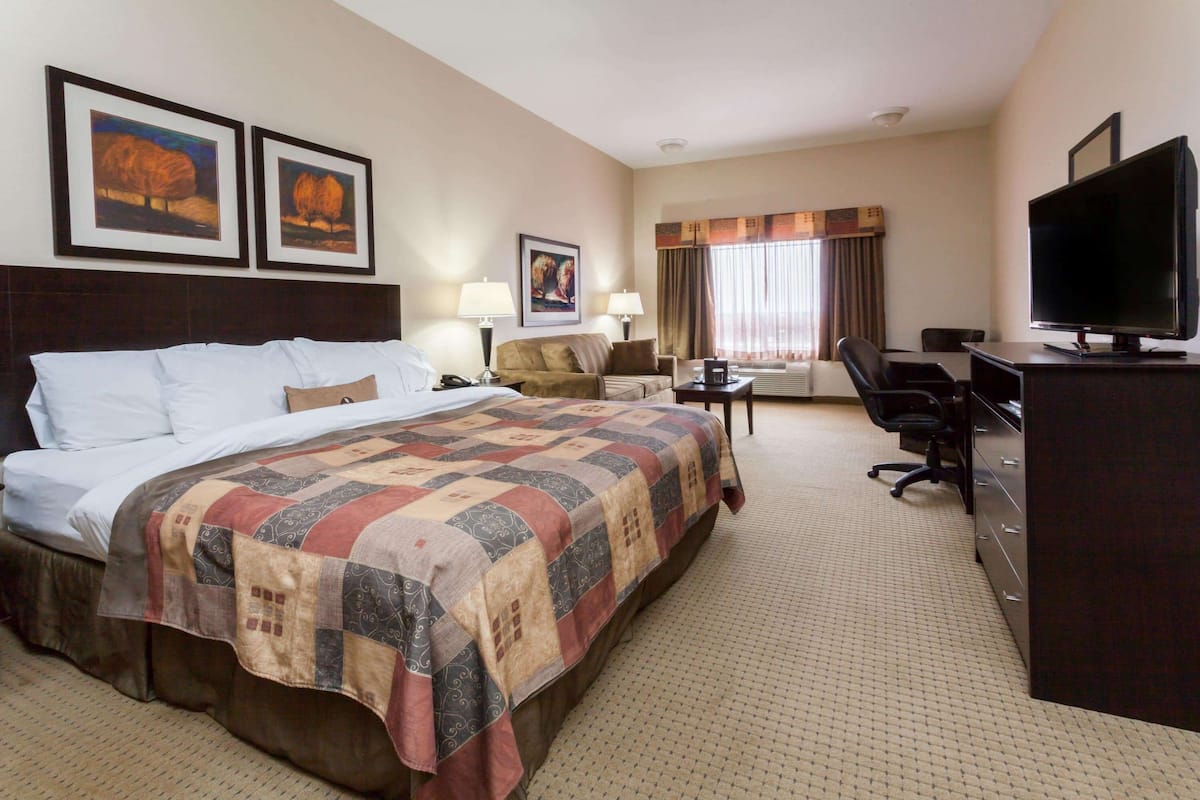 A hotel room with a large bed, a desk with a computer, a TV, and two framed pictures on the wall.