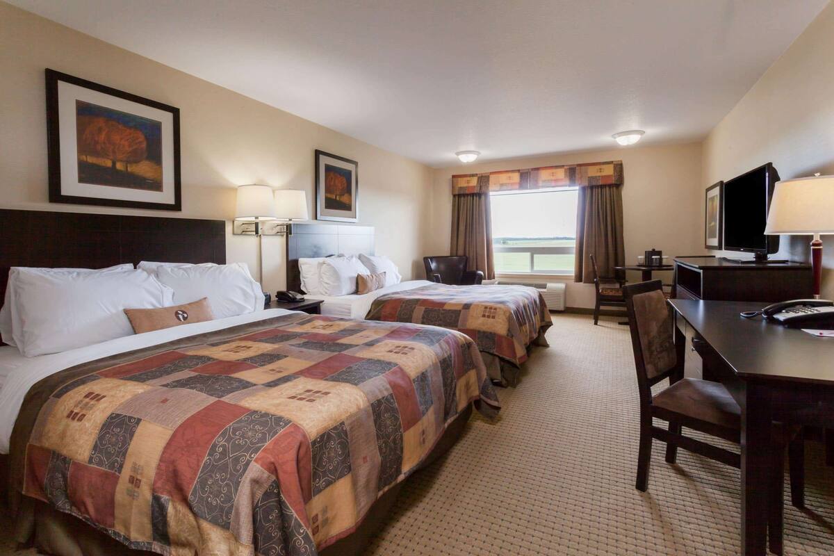 A hotel room with two beds, a desk, a chair, a TV, and a window with curtains.