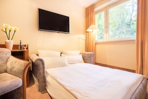 A hotel room with a bed, a television, a lamp, a chair, and a vase with flowers.