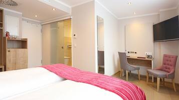Una habitación de hotel con cama, escritorio, silla, televisor y armario.