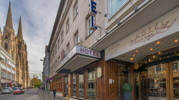 Un hôtel avec une enseigne indiquant «
HÔTEL
» et «
MARBURGER HOTEL
», situé devant un bâtiment historique doté de tours à flèche.