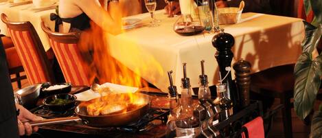 Un interior de restaurante con una mesa para dos, una zona de bar con botellas y un tablero de menú con opciones de comida.