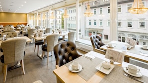 A modern restaurant with leather chairs, wooden tables, and large windows offering city views. - Hotel Marburger Hof (Marburg)